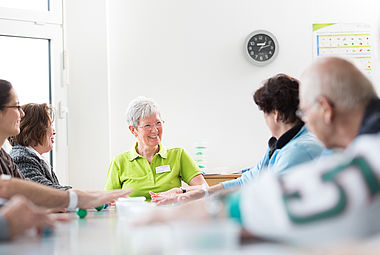 Eine Mitarbeiterin der Therapiedienste Volmarstein sitzt mit mehreren Patienten an einem Tisch. Sie kneten gemeinsam.